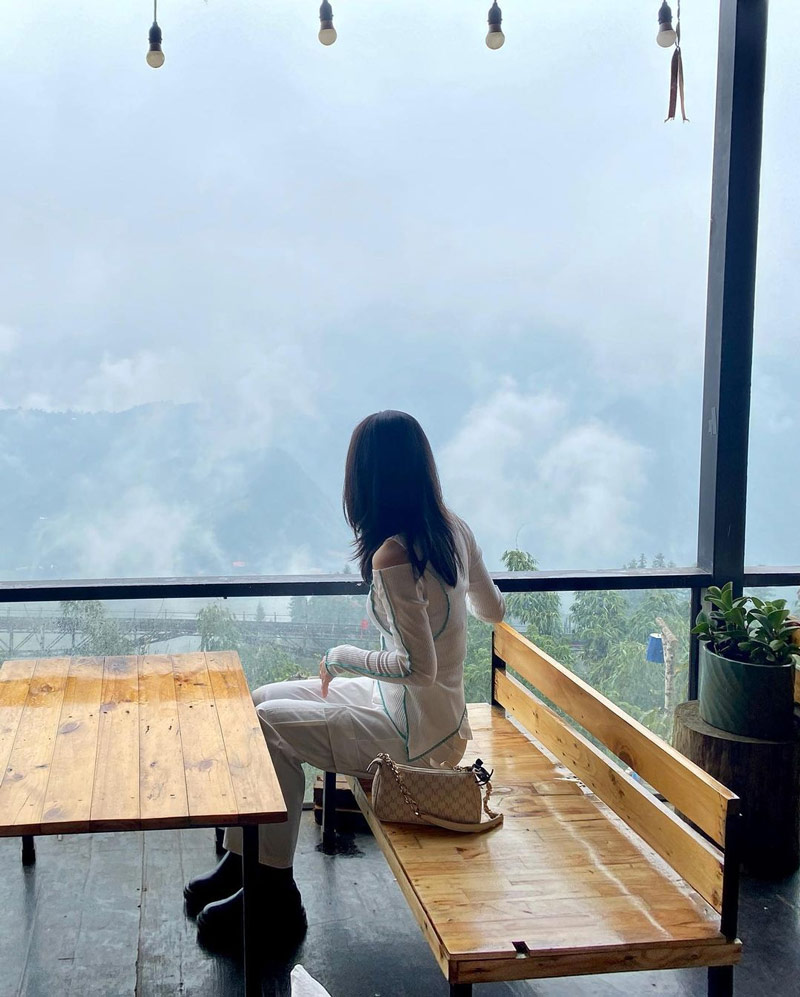 Du khách nữ ngắm mây trôi hững hờ qua ô cửa kính tại Lá Đỏ Homestay 