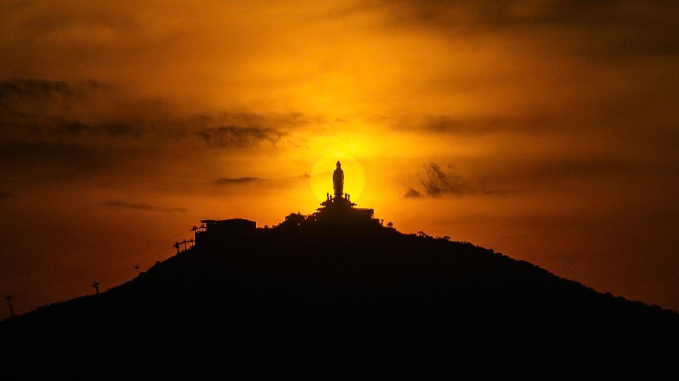 Ánh hoàng hôn lặn sau lưng tượng Phật Bà Tây Bổ Đà Sơn trên đỉnh núi.