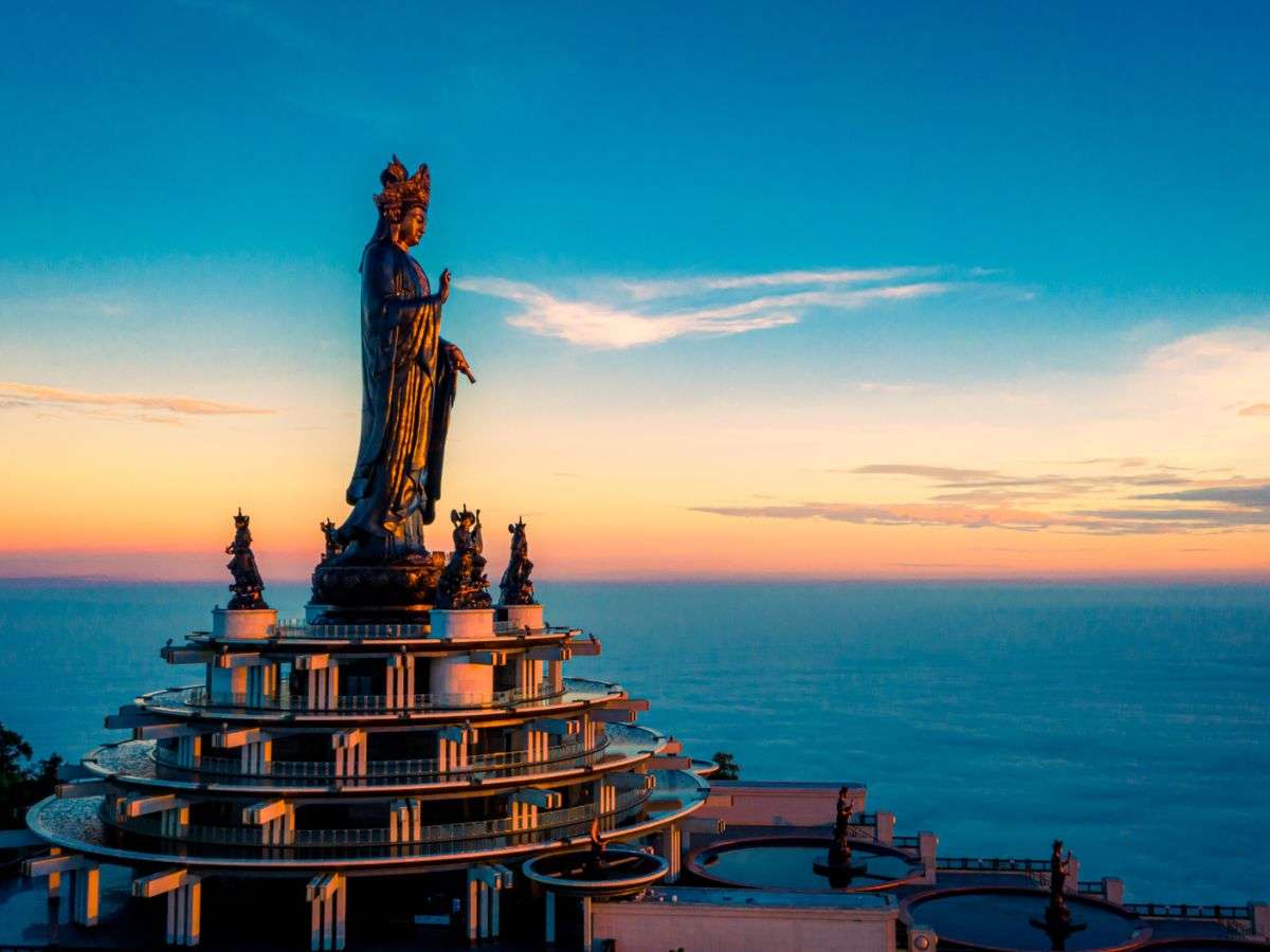 Tượng Phật Bà Tây Bổ Đà Sơn nổi bật giữa sắc hoàng hôn trên đỉnh núi.